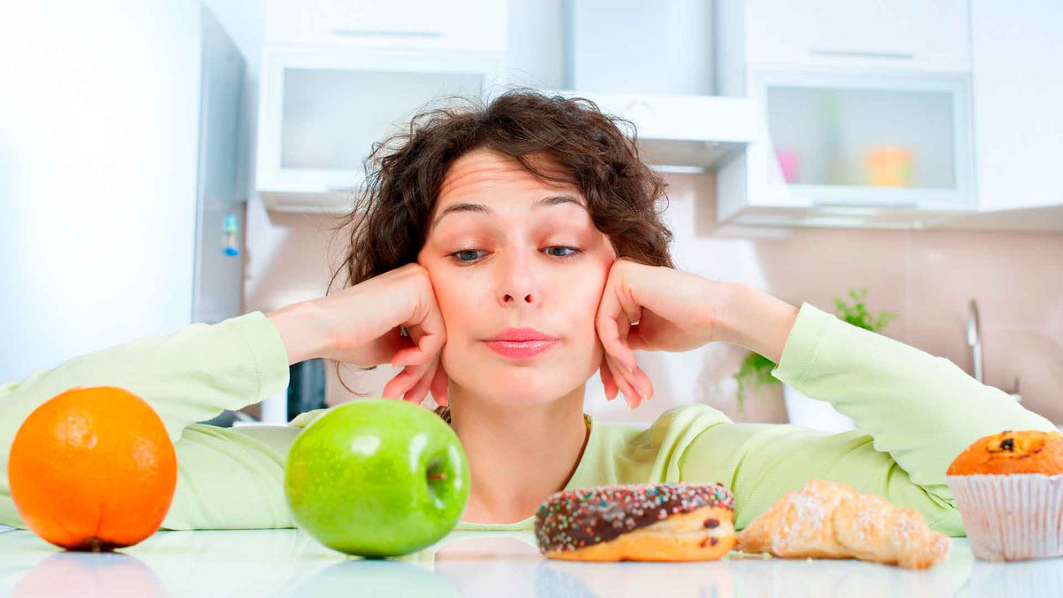 Eine Frau hat vor sich eine Orange, einen grünen Apfel und Gebäck wie Donuts liegen