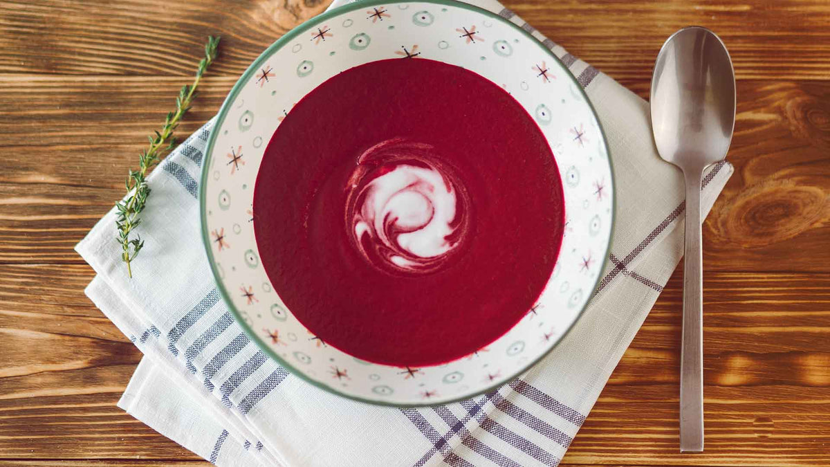 Schön angerichtete Suppe mit Roter Beete und Möhren und einem Schuss Crème fraîche zum Verfeinern. Neben der Suppenschüssel ist ein Suppenlöffel