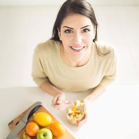 Eine junge Frau isst einen Obstsalat und schaut nach oben in die Kamera