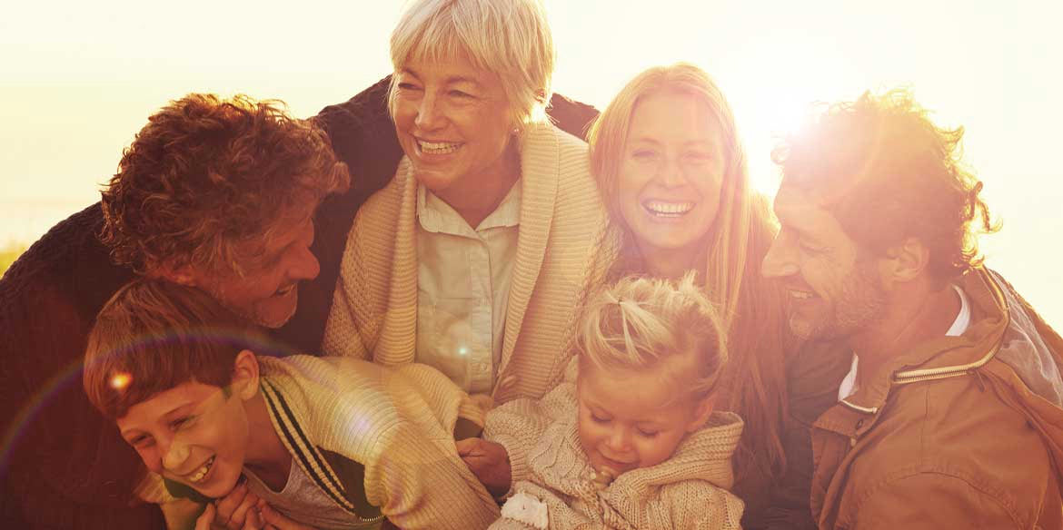 Eine glückliche sechsköpfige Familie lächelt und lacht im warmen Sonnenlicht.