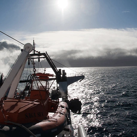 Ein Rettungsboot auf dem Deck eines Schiffes blickt bei strahlendem Sonnenschein und bewölktem Himmel auf den Ozean.