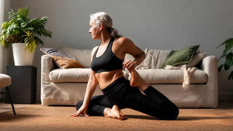 Eine Frau mittleren Alters macht eine Yogaübung im Wohzimmer vor dem Sofa