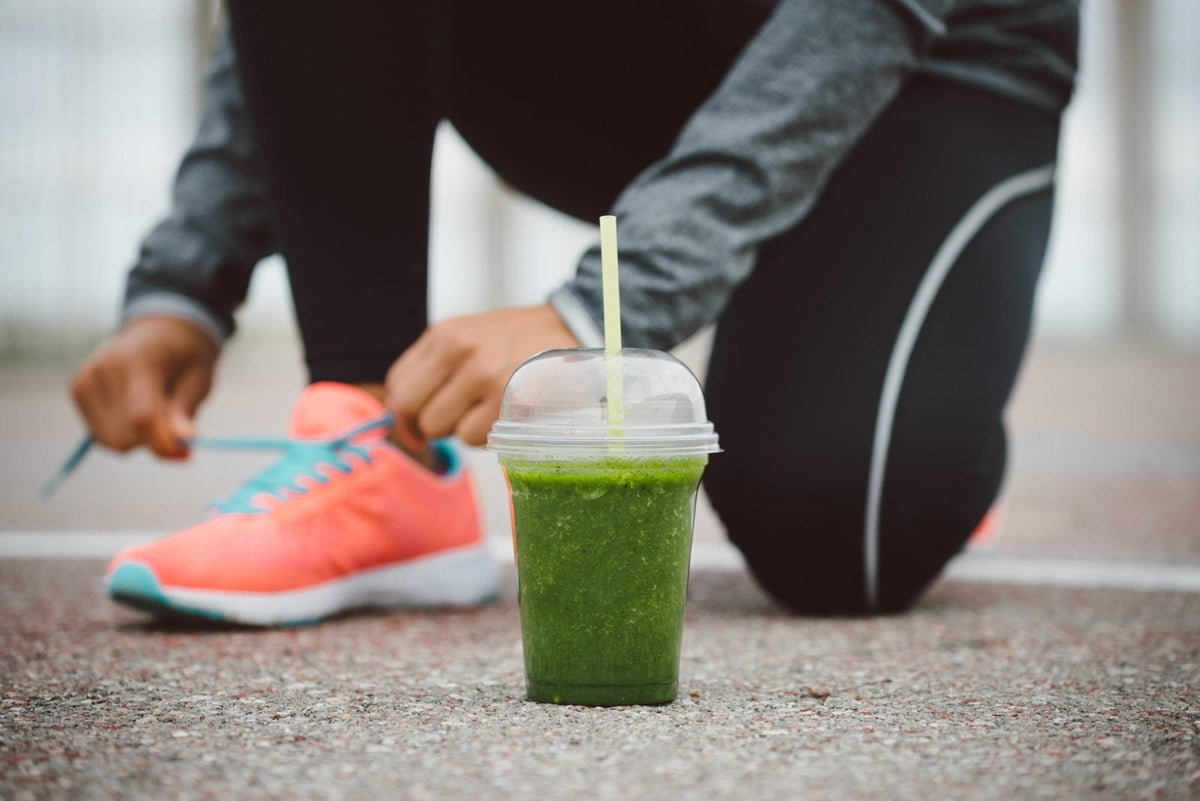 EIne Frau schnürt sich die  Sportschuhe. Vor ihr ein grüner Smoothie
