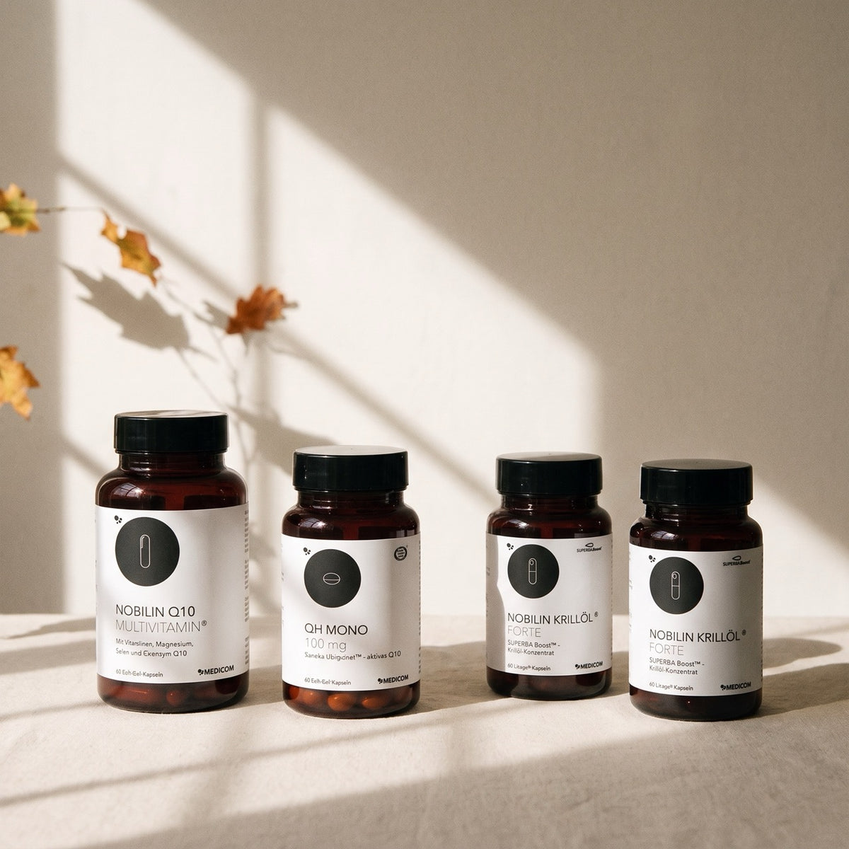 Vier bernsteinfarbene Flaschen des Nahrungsergänzungsmittels Medicom Herbst-Routine Bundle stehen auf einer Fläche in einer Reihe.
