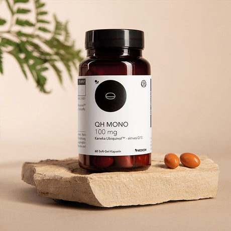 Eine Flasche „Gratis QH Mono 100 mg“ von Medicom, auf der Softgel-Kapseln auf einem Stein abgebildet sind, im Hintergrund ist eine Pflanze zu sehen.