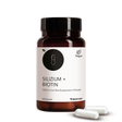 Die Produktdose von Silizium + Biotin in der Vorderansicht und zwei Kapseln vor der Produktdose