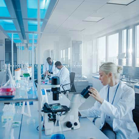 Wissenschaftler in Laborkitteln arbeiten mit Mikroskopen und Geräten in einem hellen, modernen Labor.